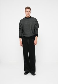 Maglione a righe nere e grigie con collo rotondo, abbinato a pantaloni neri larghi. L'outfit presenta una vestibilità comoda e una texture morbida.