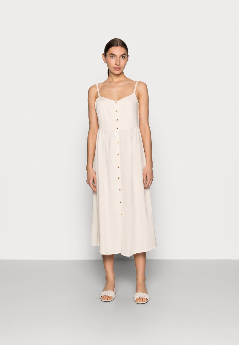 Leicht beiges, ärmelloses Kleid mit einem Knopfverschluss vorne, einem figurbetonten Oberteil und einem fließenden Rock. Glattes Material und ein schlichtes Design.