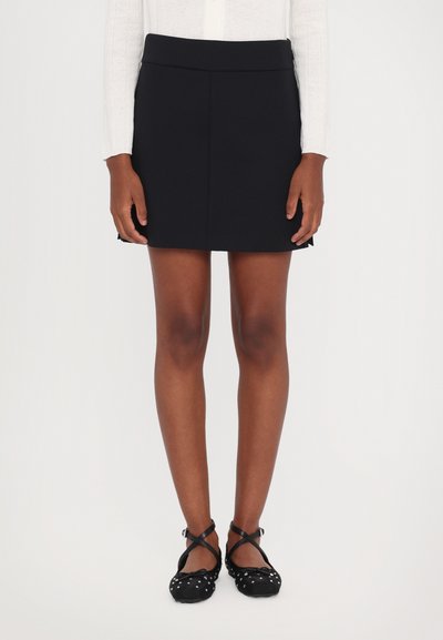 Jupe mini noire en tissu lisse, taille cintrée et design simple. Accompagnée de ballerines noires à pois avec des brides croisées.