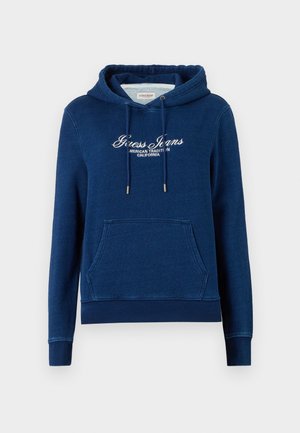 Tmavomodrá mikina s kapucňou obsahujúca predné klokánkové vrecko, šnúrku na kapucni a biely nápis „Guess Jeans American Tradition California“ na hrudi.