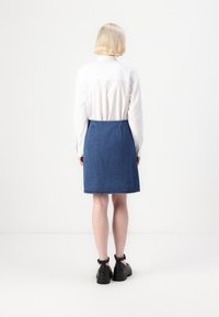 Denimskjørt med rett design, midt på låret lengde, og rå kant. Kombinert med en hvit skjorte med knapper og svarte sko.