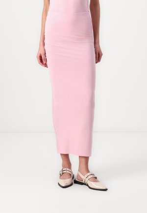Light pink, form-fitting maxi skirt made of stretchy fabric, featuring side ruching and a smooth, solid design. Worn with light-colored shoes.