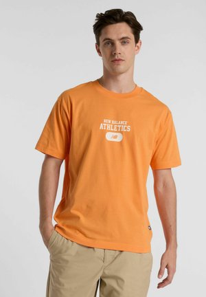 T-shirt en coton orange avec un graphisme "NEW BALANCE ATHLETICS" en blanc, manches courtes, col rond et coupe décontractée.