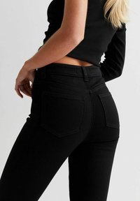 Jeans neri a vita alta in denim, con una silhouette aderente, due tasche posteriori e dettagli di cucitura discreti.