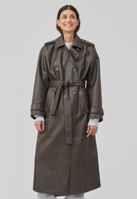 Mørkegrønn faux skinn trench coat med belte i livet, dobbeltknappede knapper og skulderklaffer, med en glatt og jevn tekstur.