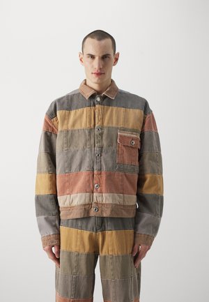 Knopenjack met een patchworkontwerp met horizontale strepen in gedempte tinten bruin, oranje en grijs; detail van de voorzak.