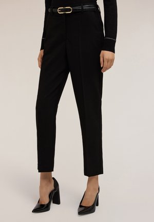 Pantalons noirs ajustés avec une coupe slim, un tissu lisse et une ceinture noire sécurisée avec une boucle en or. Assortis à des chaussures à talons hauts noires.