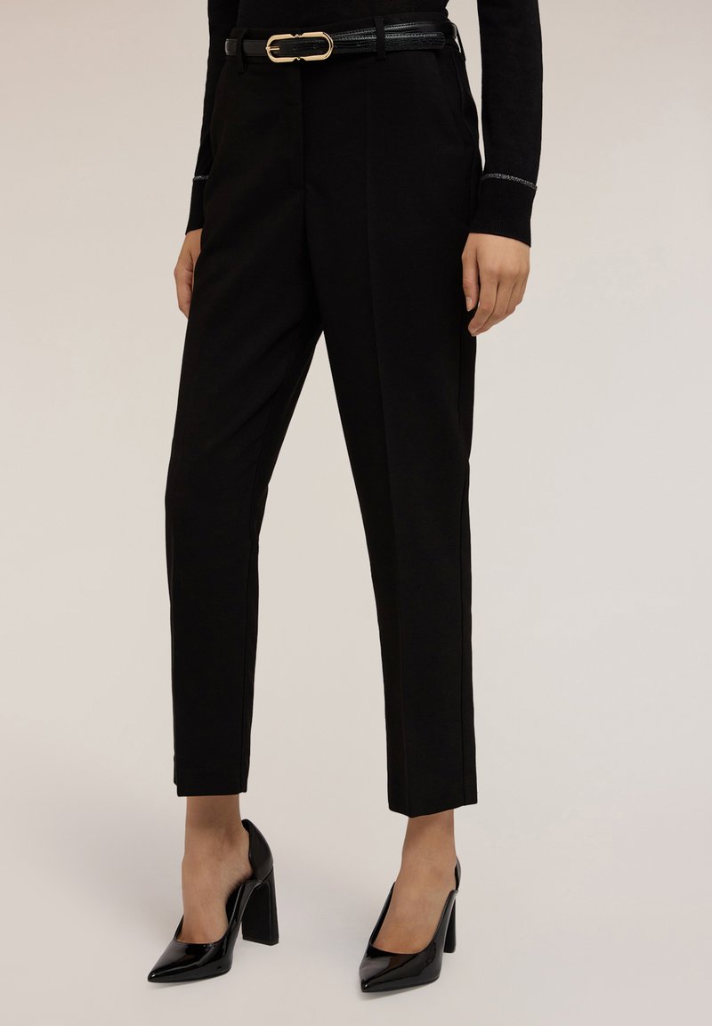 Zwarte op maat gemaakte broek met een slim fit, gladde stof en een beveiligde zwarte riem met een gouden gesp. Gepaard met zwarte hoge hakken.