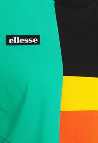 Tela en bloques de color verde, negro, amarillo y naranja con un parche negro bordado con la palabra "ellesse" en letras blancas.