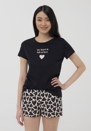 T-shirt nera con la scritta "il mio cuore è pieno d'amore" in rosa, abbinata a pantaloni corti con un motivo di cuori neri su uno sfondo chiaro.
