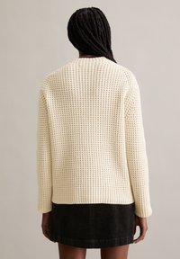 Cremefarbener gestrickter Pullover mit strukturiertem Muster, Rundhalsausschnitt und langen Ärmeln, kombiniert mit einem schwarzen Kordrock in Mini-Länge.