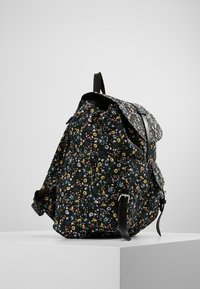 Sac à dos à imprimé floral avec une base noire ornée de petites fleurs multicolores, en tissu, doté de bretelles ajustables et d'un rabat supérieur pliant.