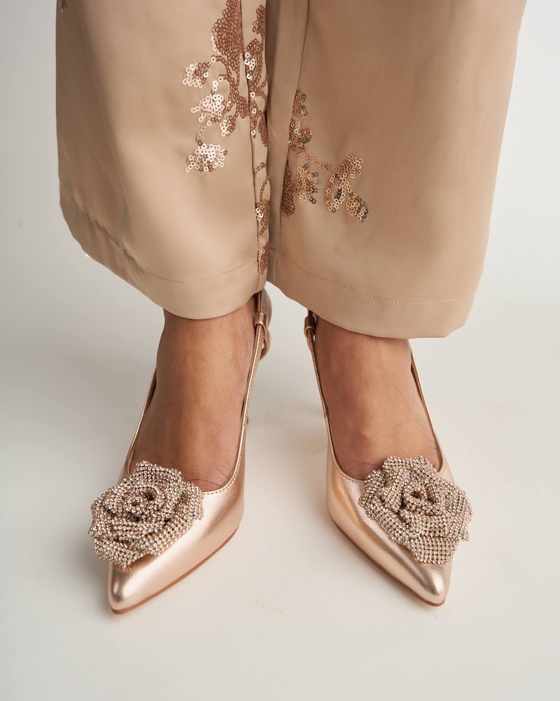 Scarpe con tacco alto color rosa dorato con punta affusolata, decorate con un accento di rosa in perline, abbinate a un outfit beige con paillettes.