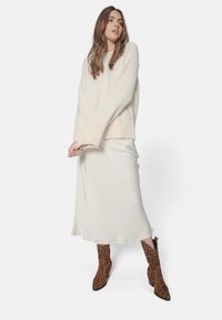 Pulover oversized de crem deschis cu margine ribbată, asociat cu o fustă albă din satin fluid și botine călcate cu model leopard maro.