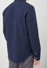 Laivastonsininen pitkähihaisen paidan, jossa on napilliset kalvosimet, tavallinen kaulus ja kaareva helma. Kangas näyttää sileältä ja siinä on vähän pintakuvioita.