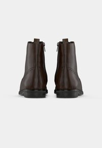 Καφέ δερμάτινες μπόOtike μπότες μέχρι τον αστράγαλο με λεία υφή, που διαθέτουν φερμουάρ στο πλάι και διακοσμητικές τρυπάνες στο πάνω μέρος. Μαύρη επίπεδη σόλα.