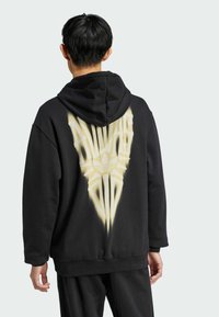 Juodas džemperis su dideliu geltonu grafiniu piešiniu nugaros pusėje, vaizduojančiu stilizuotą „ALWAYS“ tekstą ir Adidas logotipą. Pagamintas iš medvilnės mišinio, laisvas pjūvis.