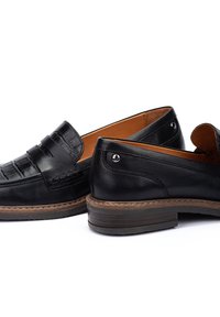 Mocassins en cuir noir avec un design de bout texturé, semelle marron et coutures contrastantes. Présente un dos lisse et des accents décoratifs en argent.
