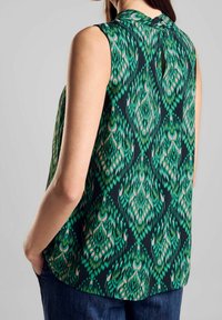 Ärmlös topp i lättviktsmaterial med en grön, flerfärgad design på en mörk bakgrund och en subtil detalj med öppning baktill.