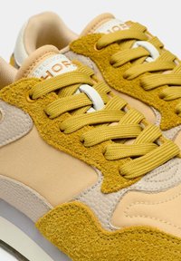 Zapatillas que combinan cuero beige, ante y detalles texturizados en amarillo. Cordones amarillos, cuello acolchado y un diseño estampado a lo largo de la suela.