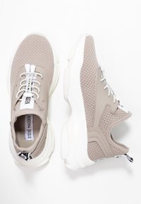 Baskets en maille beige clair avec semelles épaisses blanches, lacets blancs et gris, et logo "Steve Madden" sur la languette et la semelle intérieure.