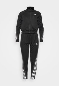 Survêtement Adidas noir avec des bandes blanches sur les manches et le pantalon, veste zippée, taille élastique et logos Adidas sur la poitrine et la cuisse.