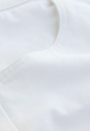 Vitt tyg med en slät yta, med en rundad halsringning och precisa sömnadsdetaljer. Materialet ser lätt och mjukt ut.