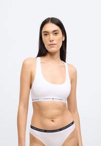 Fehér sportmelltartó széles, "TOMMY HILFIGER" feliratú piros és kék logószalaggal. Simább anyag, kerek nyakkivágás és vastag vállpántok.