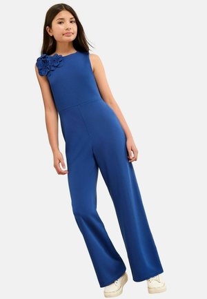 Blauwe jumpsuit met een getailleerde bovenkant en vloeiende broekspijpen. Heeft een grote bloemenaccent op de linkerschouder. Gemaakt van glad, rekbaar materiaal.