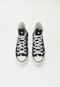 Hochschaft-Sneaker mit einem schwarzen Canvas-Obermaterial, das große pinkfarbene Punkte aufweist, weißen Schnürsenkeln und einer weißen Gummispitze.