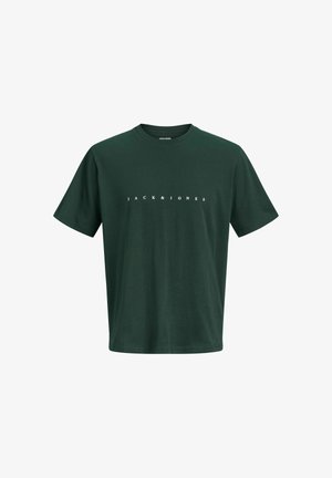 Jongen staat frontaal, draagt een geruit overhemd over een donkergroen T-shirt, een donkere spijkerbroek en beige schoenen op een effen achtergrond.