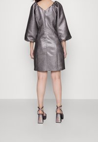 Metallinen hopeanhohtoinen shift-mekko, jossa on puffihihat ja V-mallinen selkäosa, yhdistetty mustiin, korollisiin sandaaleihin, joissa on kimalteleva viimeistely.