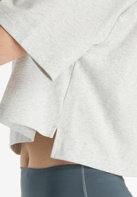 Lichtgrijze oversized t-shirt met korte mouwen, zijsplitten en een zachte, textuurvolle stof, gecombineerd met donkergrijze high-waisted leggings.