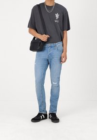 Schwarzes Grafik-T-Shirt mit Blumenmuster, hellblaue verwaschene Jeans und schwarze Sneakers mit weißen Akzenten; trägt eine kleine schwarze Tasche.