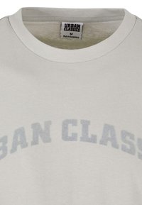 Šviesiai pilkas medvilninis marškinėlis su apvalia apykakle. Per krūtinę spausdintas užrašas "URBAN CLASSICS" ryškiomis, išblukusiomis mėlynomis raidėmis. Pridedama dydžio M etiketė.