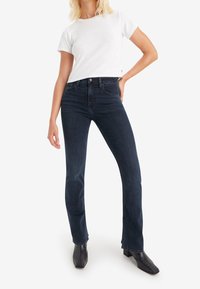 Mörkblå denim jeans med vida ben och åtsittande midja, subtila slitningar och traditionell femfickorsdesign, matchat med en vit t-shirt.