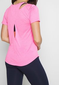 Rosa atletisk t-shirt med korta ärmar, en ryggdesign med utskärning och rundad nederkant. Kombinerad med marinblå leggins.
