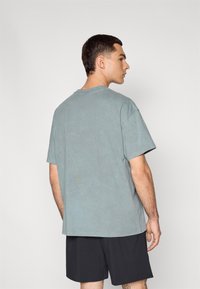 Kortærmet t-shirt med rund hals i falmet teal-stof, afslappet fit, med synlige sømdetaljer, parret med sorte shorts.