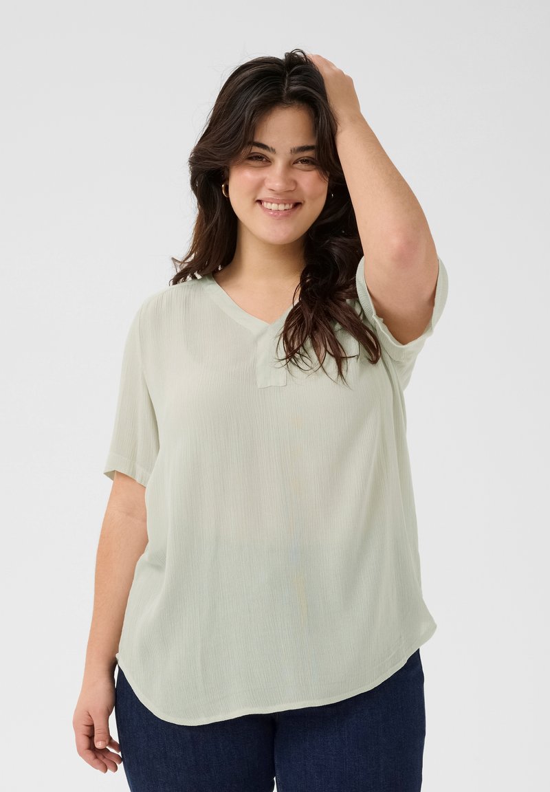Light green short-sleeve blouse with a V-neck and a slightly curved hem, made from a textured, flowing fabric.