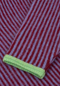 Gebreide stof met rode en lichtblauwe strepen en een zachte structuur. Groene rand aan de manchet zorgt voor een contrasterend detail.