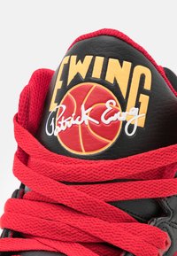 Baskets en cuir noir avec lacets rouges, grand logo "EWING", un logo de basketball rouge, et la signature "Patrick Ewing".