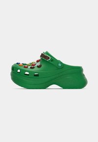 Green clogs featuring decorative M&M's and a brown strap, made from textured material with ventilation holes on the sides.