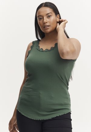 Grünes geripptes Tanktop mit gewelltem Spitzenbesatz am Ausschnitt und abgerundetem Saum, kombiniert mit schwarzen eng anliegenden Hosen. Sanfte Textur.