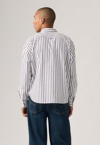 Hvit og marineblå stripet skjorte med lange ermer, knappe mansjetter og krage. Stoffet fremstår som glatt, med en avslappet passform og ryggdetalj.