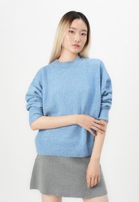Maglione azzurro chiaro a maglia con polsini e orlo a coste, maniche corte, abbinato a una gonna grigia a maglia. Texture morbida e vestibilità rilassata.