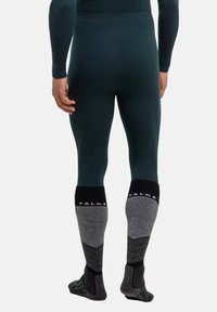 Thermounterwäsche für Herren in Dunkelgrün, figurbetontes Design; kombiniert mit grauen Socken mit schwarzen Akzenten und Zickzackmuster an den Sohlen.