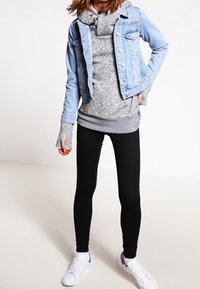 Farkkutakki, jossa on metallinapit, harmaa huppari korkealla kauluksella ja mustat legginsit. Jalkineet: valkoiset lenkkarit sinisin yksityiskohdin.