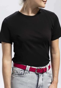 Schwarzes T-Shirt mit kurzen Ärmeln und Rundhalsausschnitt. Getragen mit hellgrauen Jeans und einem leuchtend rosa Gürtel mit einer runden silbernen Schnalle.