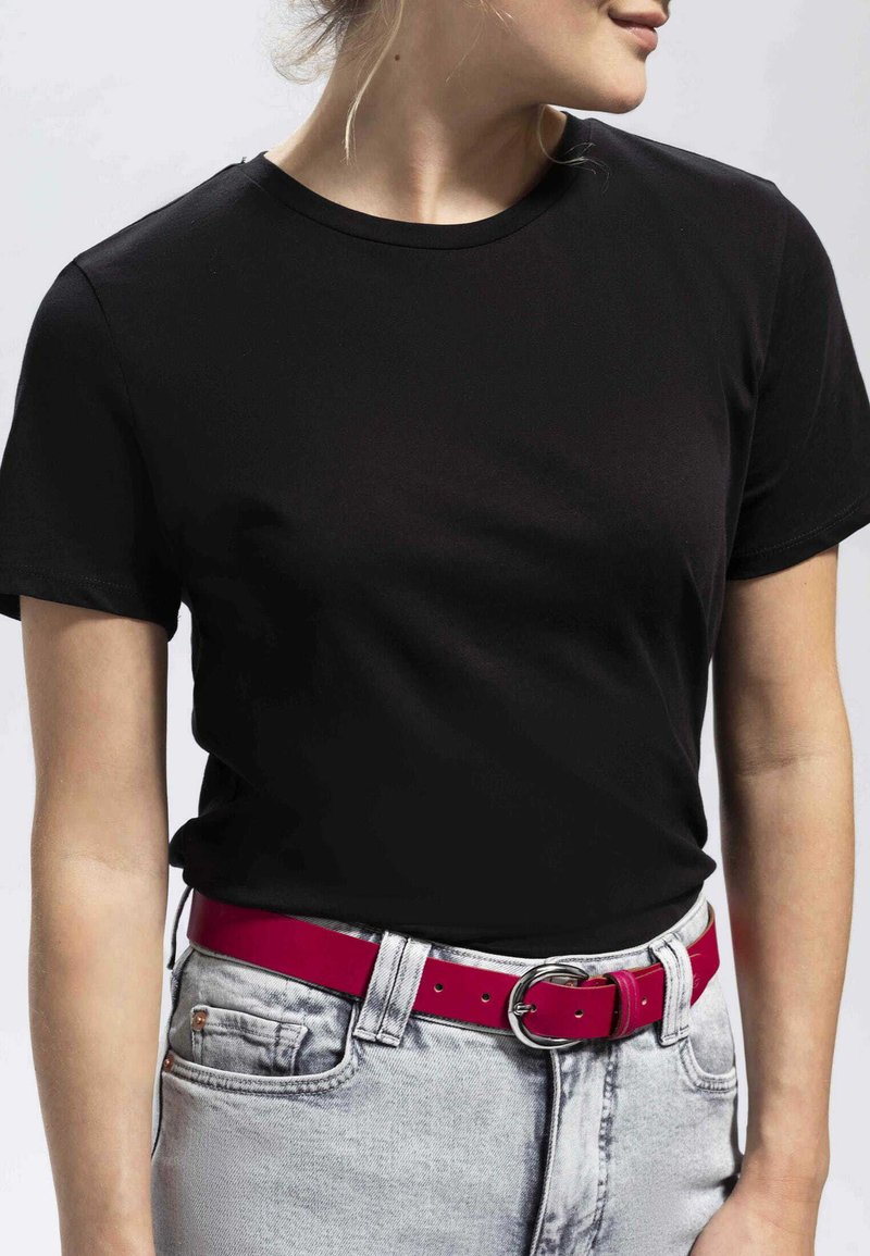 Schwarzes T-Shirt mit kurzen Ärmeln und Rundhalsausschnitt. Getragen mit hellgrauen Jeans und einem leuchtend rosa Gürtel mit einer runden silbernen Schnalle.