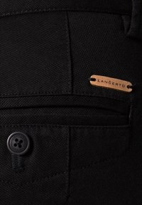 Czarna tkanina z kieszenią, czarnym guzikiem na cztery dziurki i beżową skórzaną metką z napisem "LANÇERTO" przymocowaną.